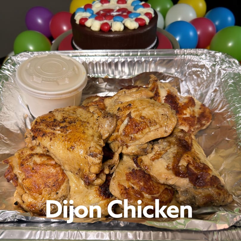 Kaimana Farm Cafe's Dijon Chicken in a foil tray with a sauce cup, a cake, and balloons.