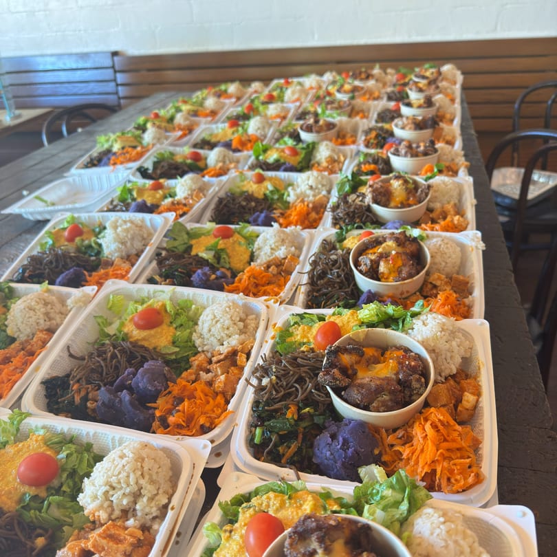 Rows of Kaimana Farm Cafe's healthy bento boxes with rice, vegetables, and meat on a wooden table.