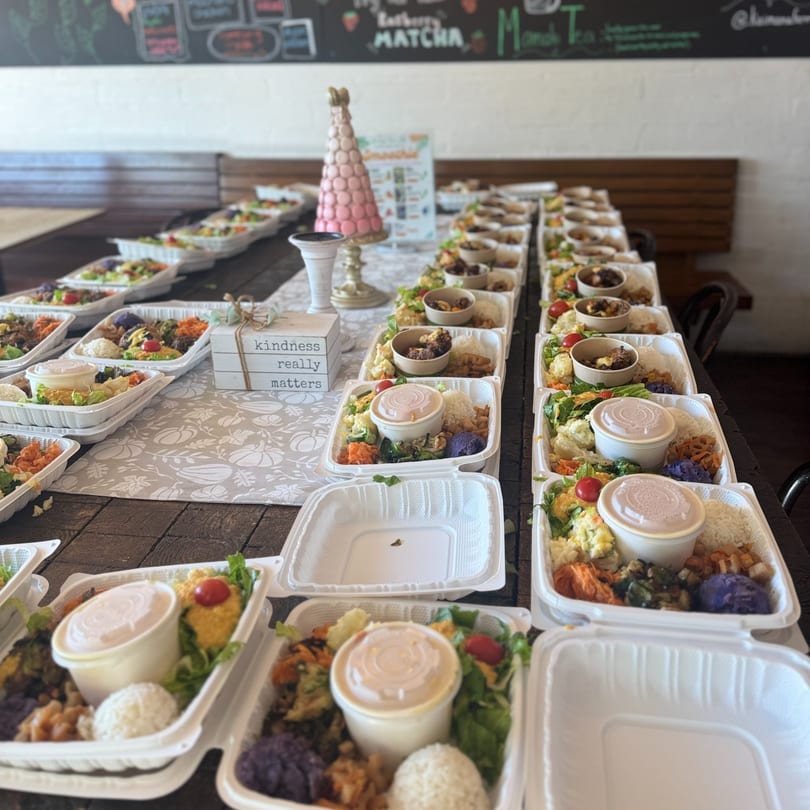 Rows of Kaimana Farm Cafe's healthy takeout meals with rice, vegetables, and protein on a long table.